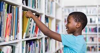 boy looking at books on library shelf